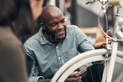Buy stock photo Shot of a handsome young man crouching down and looking at a bicycle before buying it