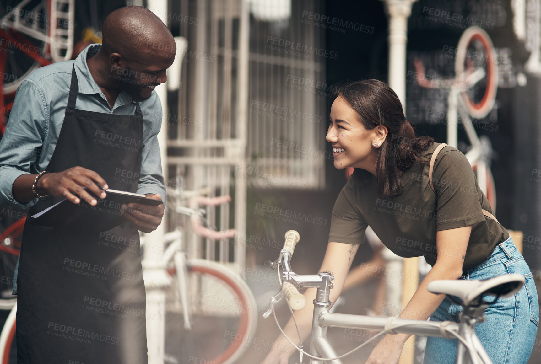 Buy stock photo Shot of a handsome young man standing outside his bicycle shop and assisting a customer