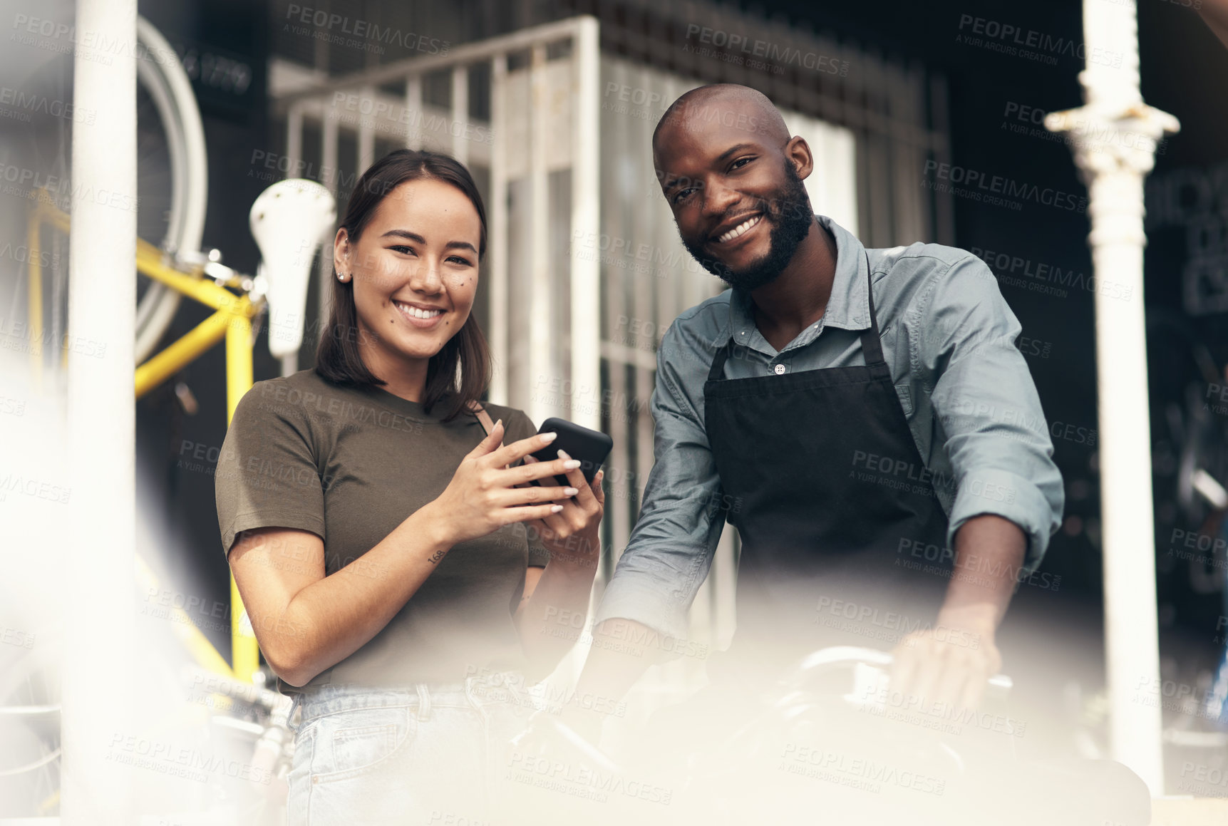 Buy stock photo Shot of a handsome young man standing outside his bicycle shop and assisting a customer
