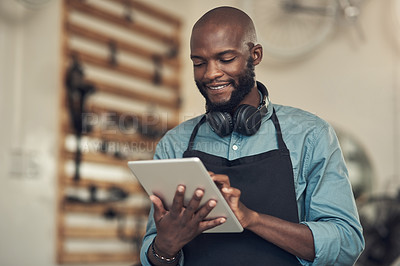 Buy stock photo Shot of a handsome young man standing alone in his bicycle shop and using a digital tablet