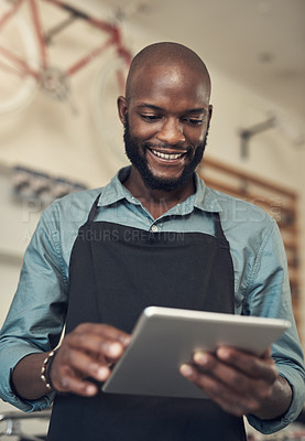 Buy stock photo Shot of a handsome young man standing alone in his bicycle shop and using a digital tablet