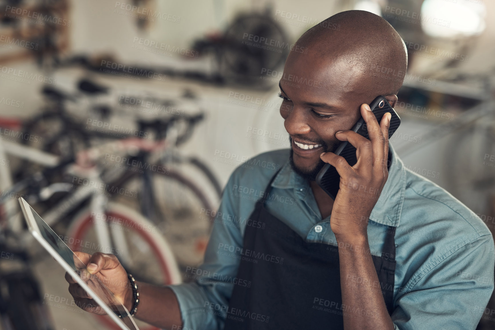 Buy stock photo Shot of a handsome young man standing alone in his bicycle shop and using technology