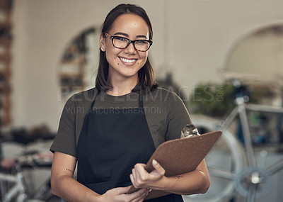 Buy stock photo Shot of an attractive young woman standing alone in her bicycle shop and holding a clipboard