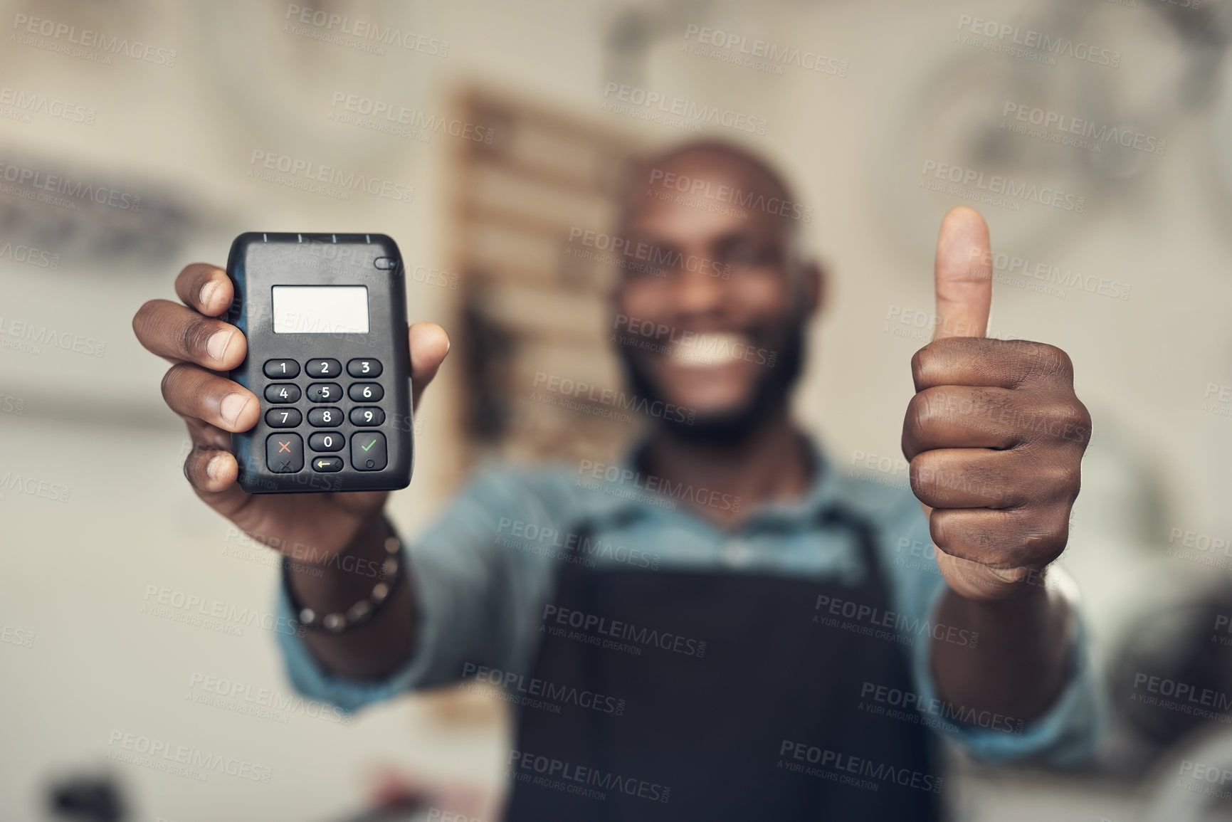 Buy stock photo Shot of an unrecognizable man standing in his shop and holding a card machine while doing a thumbs up gesture