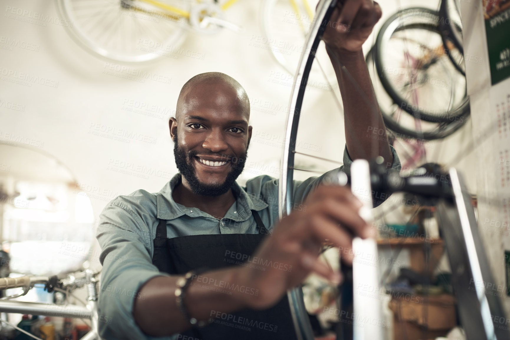 Buy stock photo Shot of a handsome young man standing alone in his shop and repairing a bicycle wheel