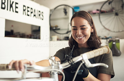 Buy stock photo Shot of an attractive young woman standing alone in her shop and repairing a bicycle