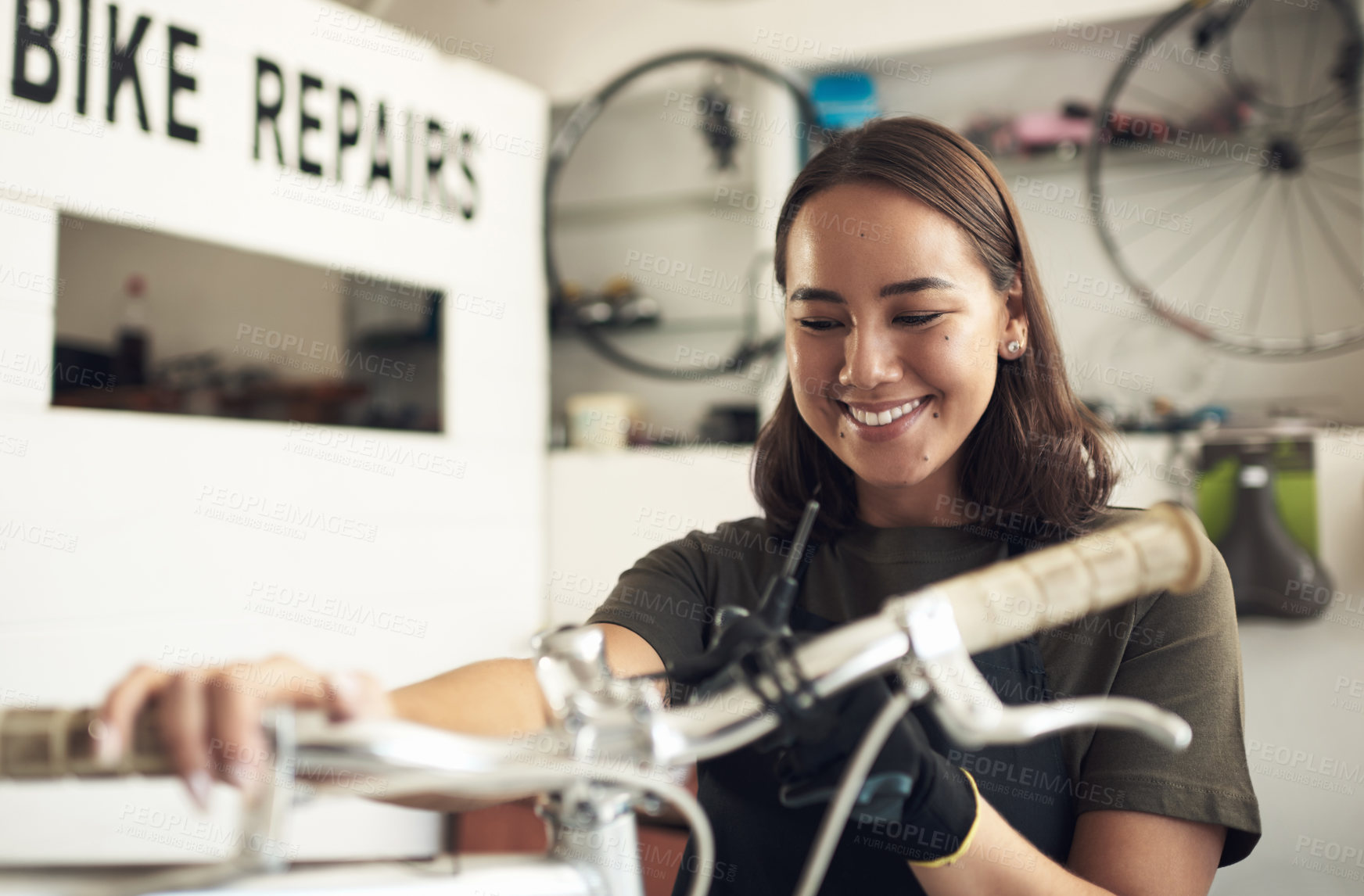 Buy stock photo Shot of an attractive young woman standing alone in her shop and repairing a bicycle