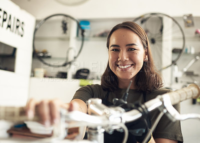 Buy stock photo Shot of an attractive young woman standing alone in her shop and repairing a bicycle