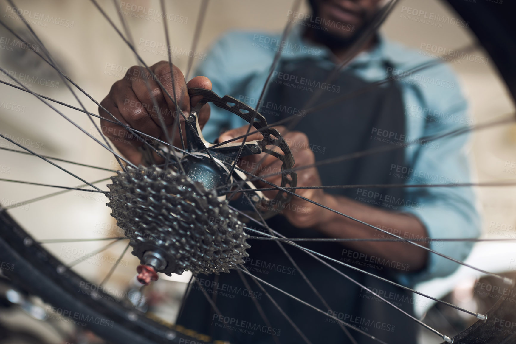 Buy stock photo Low angle shot of an unrecognizable man standing alone in his shop and repairing a bicycle wheel