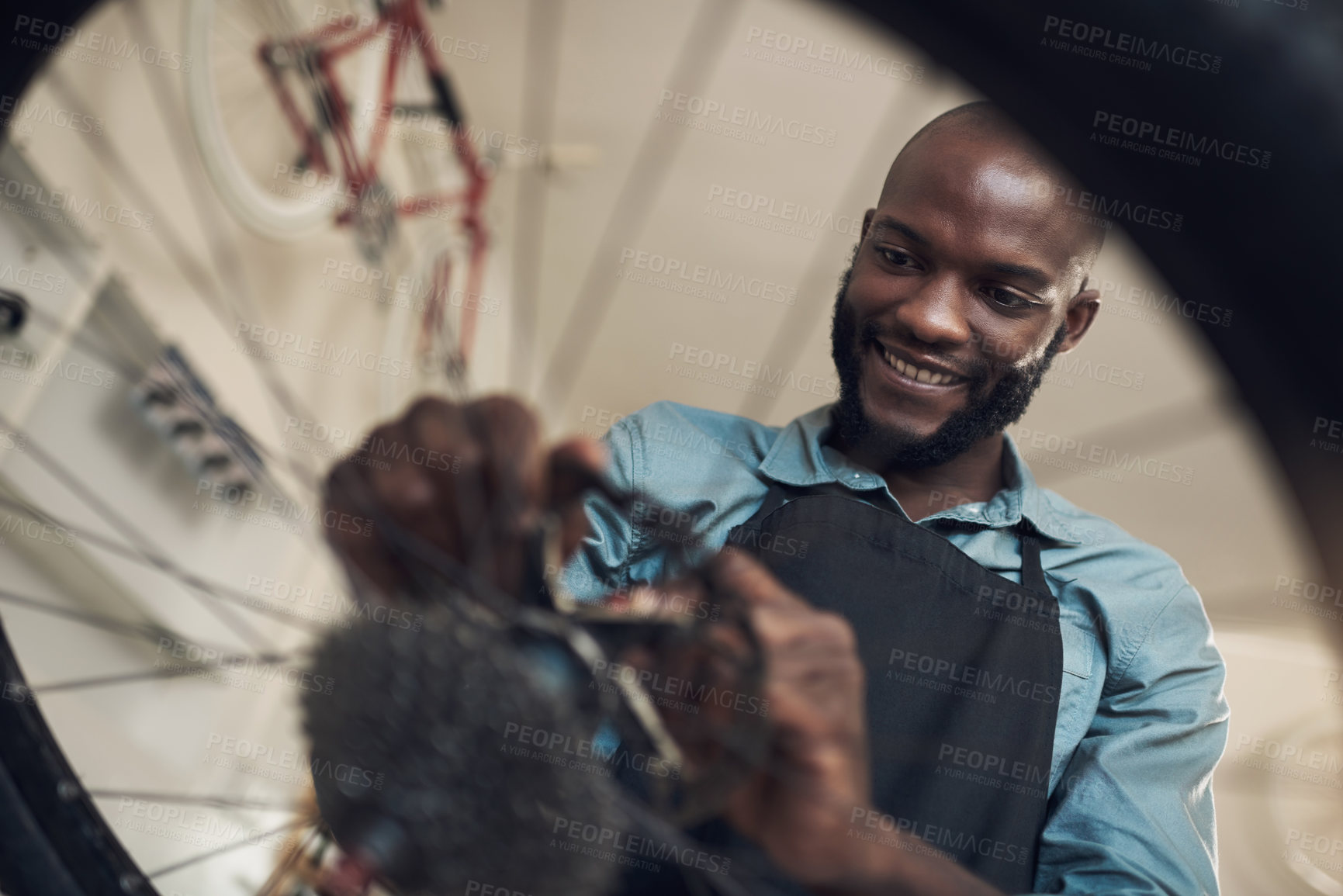 Buy stock photo Low angle shot of a handsome young man standing alone in his shop and repairing a bicycle wheel