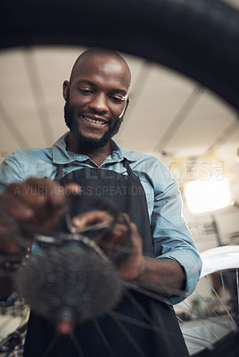 Buy stock photo Low angle shot of a handsome young man standing alone in his shop and repairing a bicycle wheel