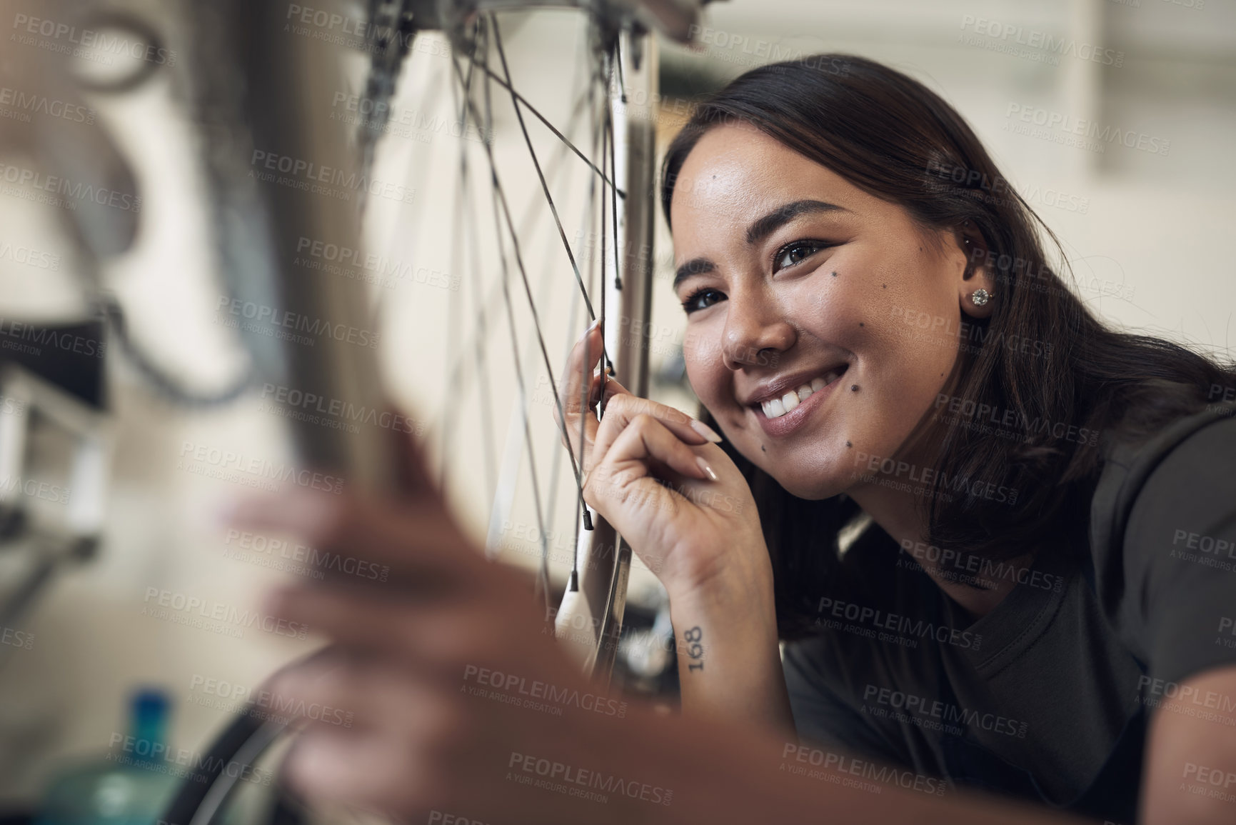 Buy stock photo Shot of an attractive young woman crouching alone in her shop and repairing a bicycle wheel
