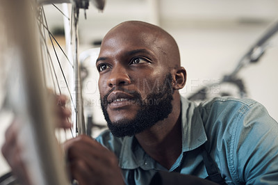 Buy stock photo Shot of a handsome young man crouching in his shop and repairing a bicycle wheel