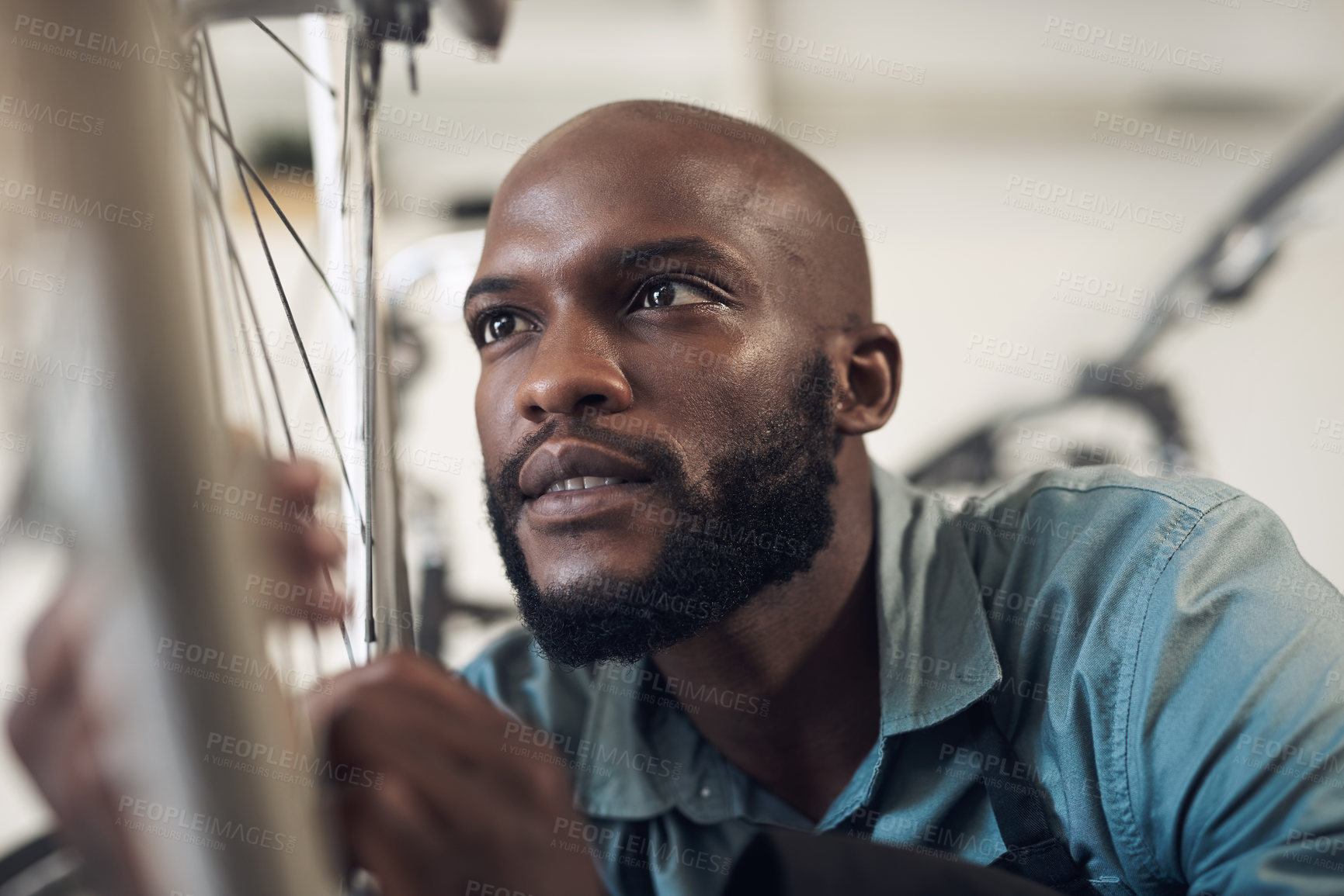 Buy stock photo Shot of a handsome young man crouching in his shop and repairing a bicycle wheel