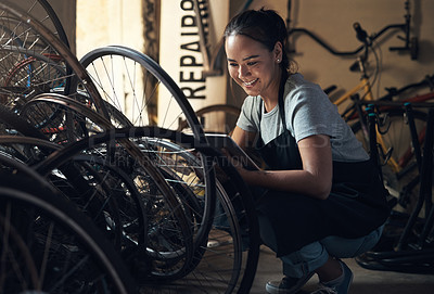 Buy stock photo Shot of a young happy young woman fixing a bike at a bicycle repair shop