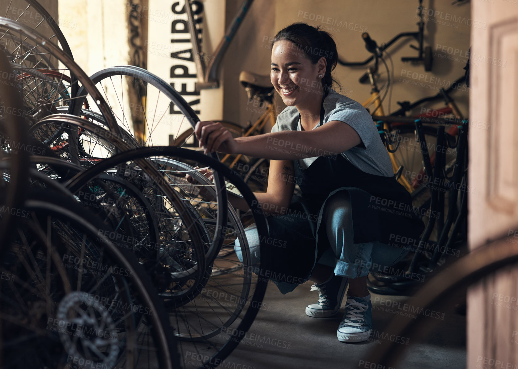 Buy stock photo Shot of a young happy young woman fixing a bike at a bicycle repair shop