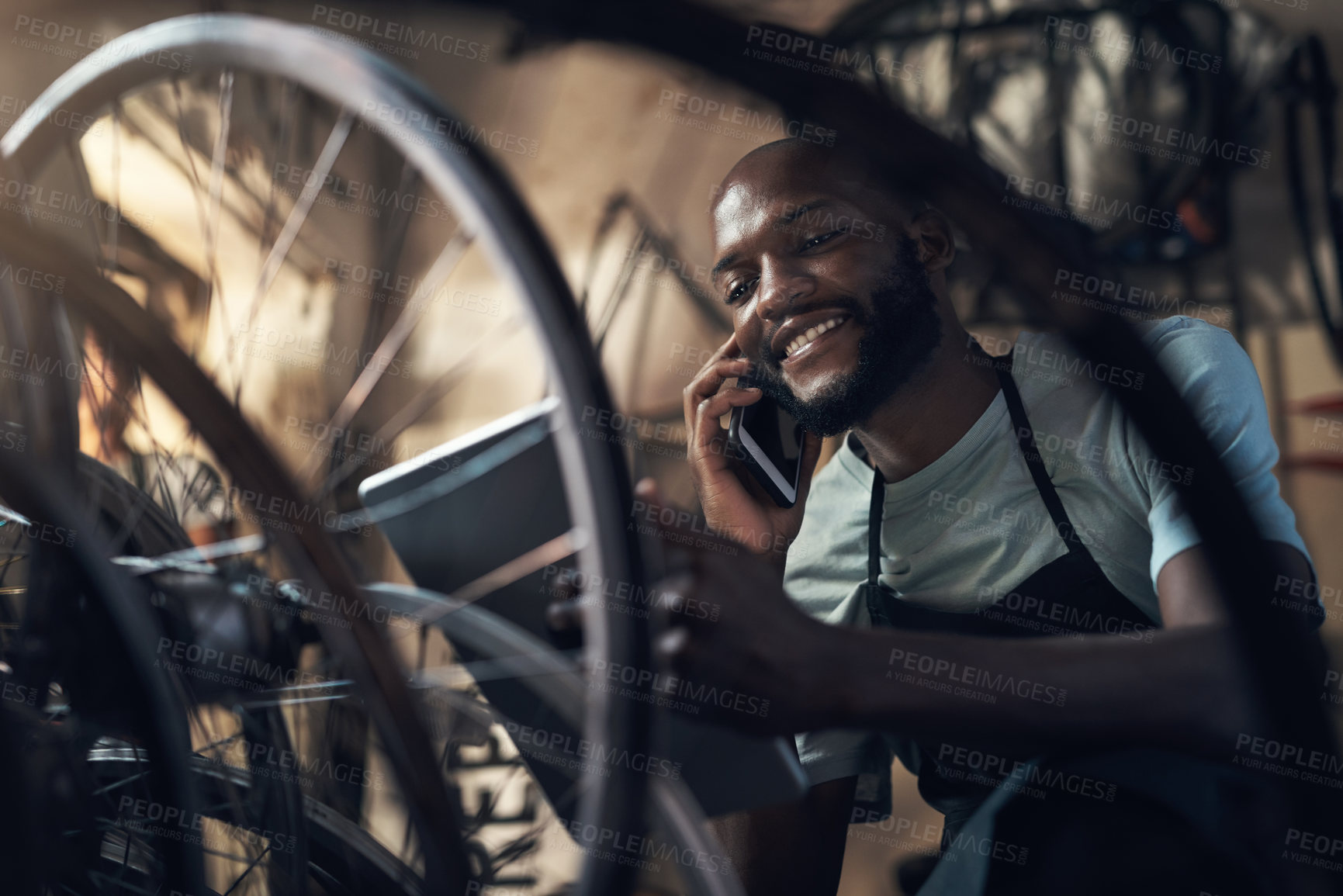 Buy stock photo Shot of a young man talking on a cellphone and browsing on a digital tablet while working at a bicycle repair shop