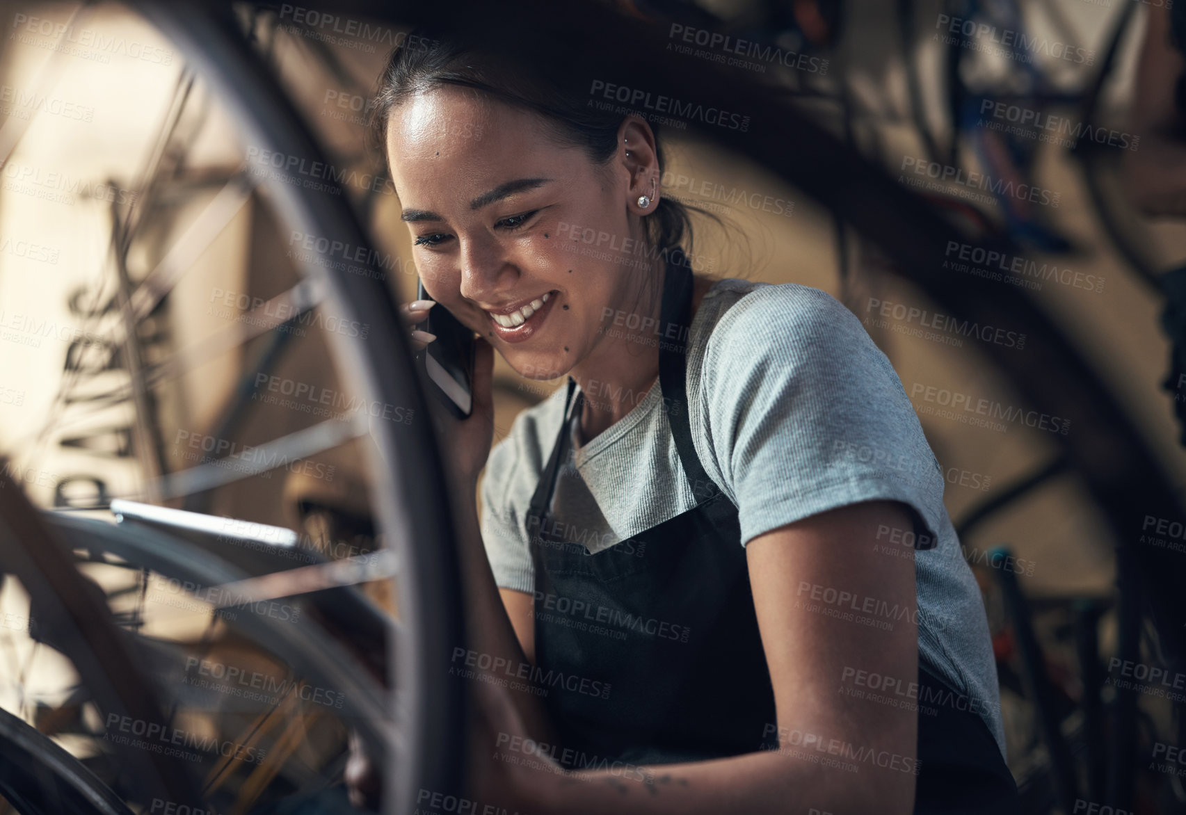 Buy stock photo Shot of a young happy young woman talking on a cellphone and using a digital tablet while fixing a bike at a bicycle repair shop