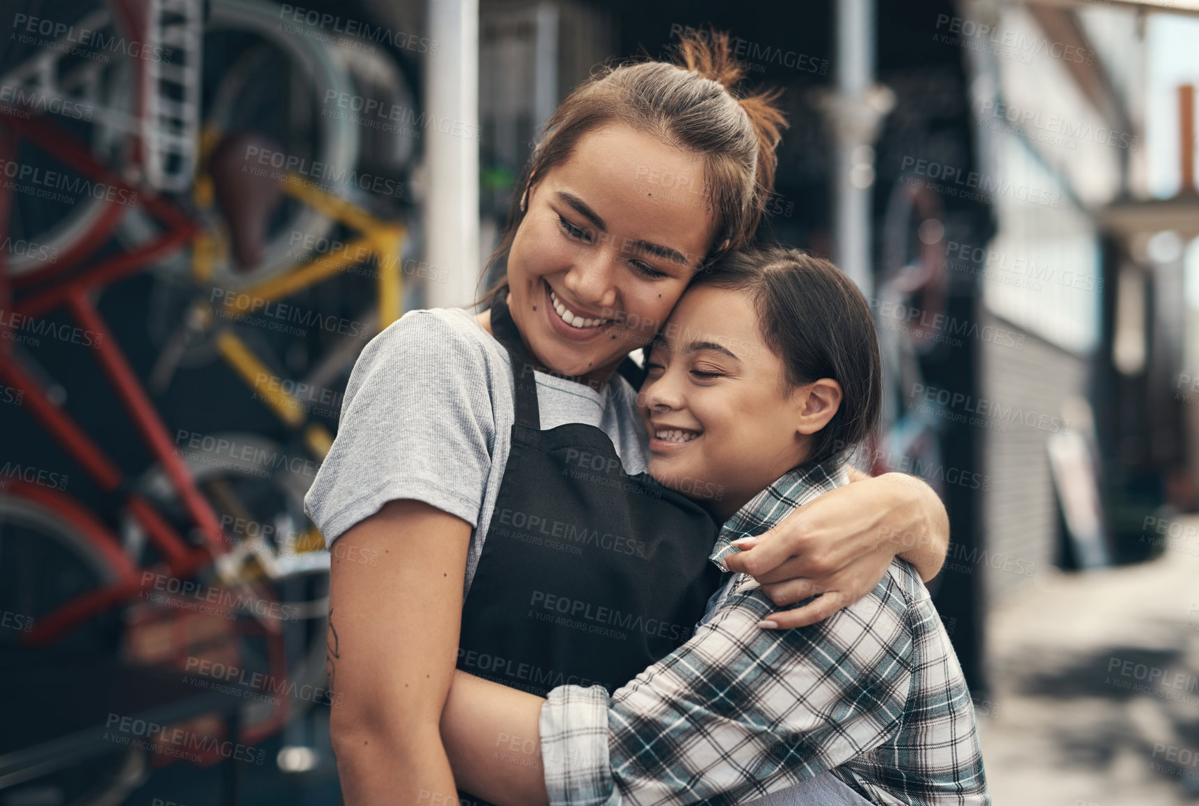 Buy stock photo Shot of two young female colleagues sharing a hug outside a bicycle repair shop