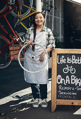 Buy stock photo Portrait of a young woman holding a bicycle wheel outside of a bicycle repair shop