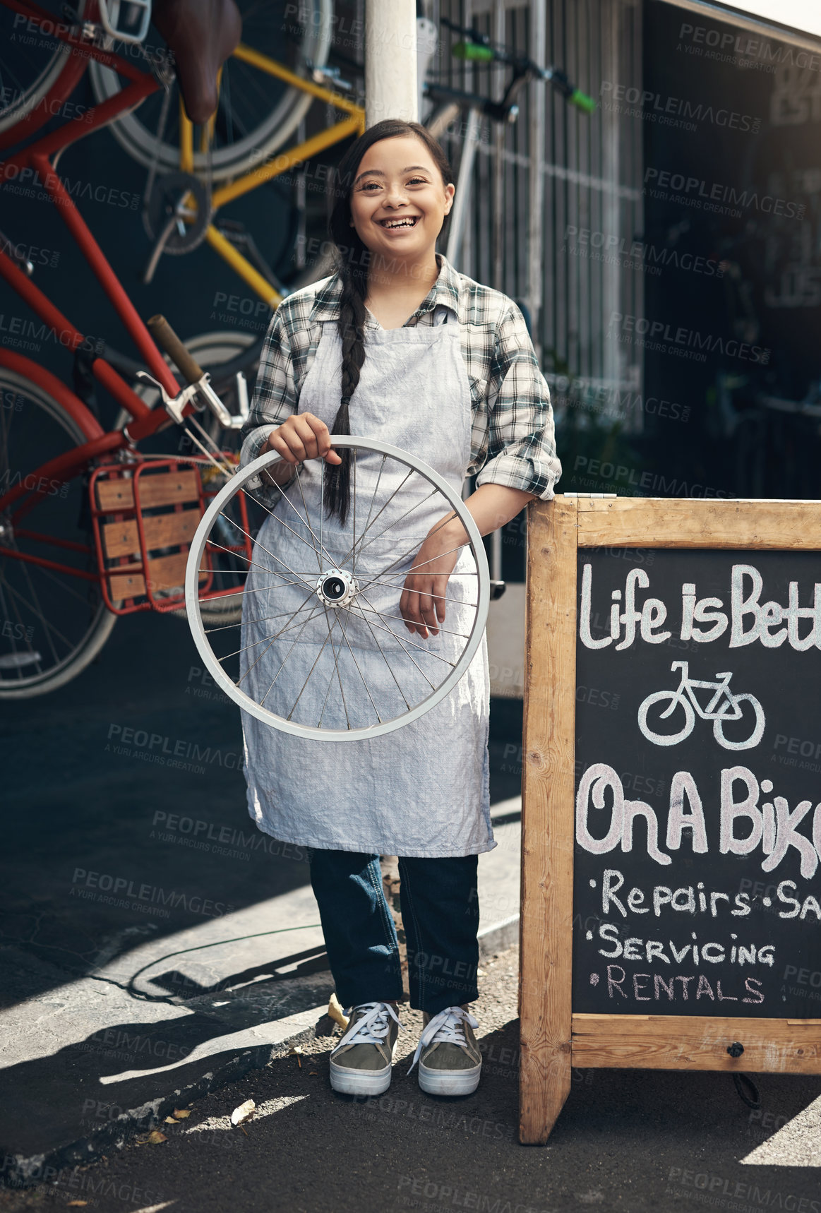 Buy stock photo Portrait of a young woman holding a bicycle wheel outside of a bicycle repair shop