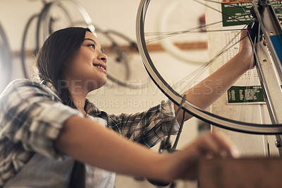 Buy stock photo Shot of a young woman fixing a bike at a bicycle repair shop