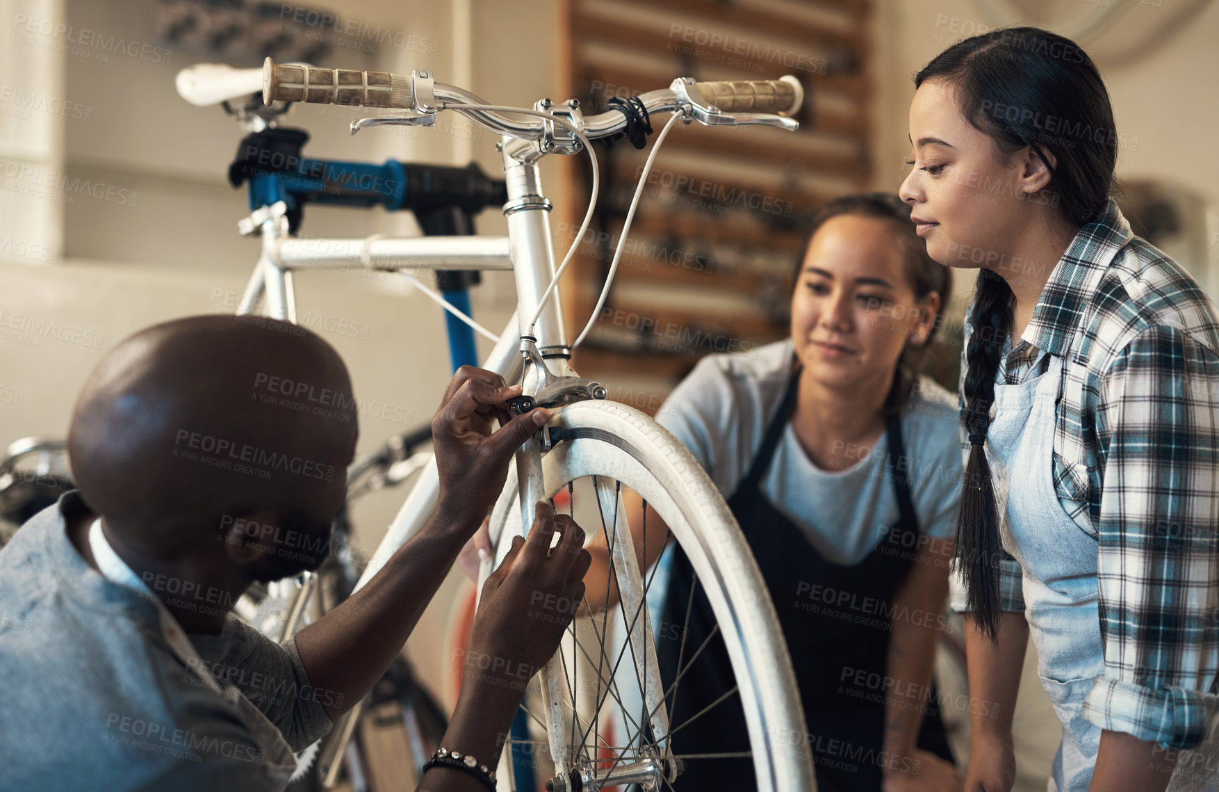 Buy stock photo Shot of three colleagues working together to fix a bike at a bicycle store