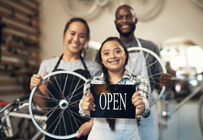 Buy stock photo Portrait of three workers standing and holding onto a bike while one displays an open sign at work