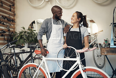 Buy stock photo Shot of two colleagues bonding while holding onto a bicycle wheel at a bicycle repair shop