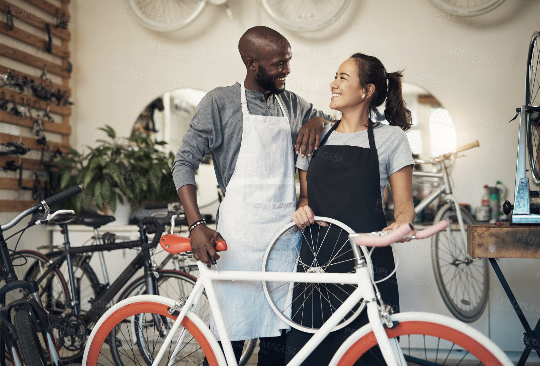 Buy stock photo Shot of two colleagues bonding while holding onto a bicycle wheel at a bicycle repair shop
