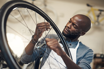 Buy stock photo Shot of a young man fixing a wheel at a bicycle repair shop