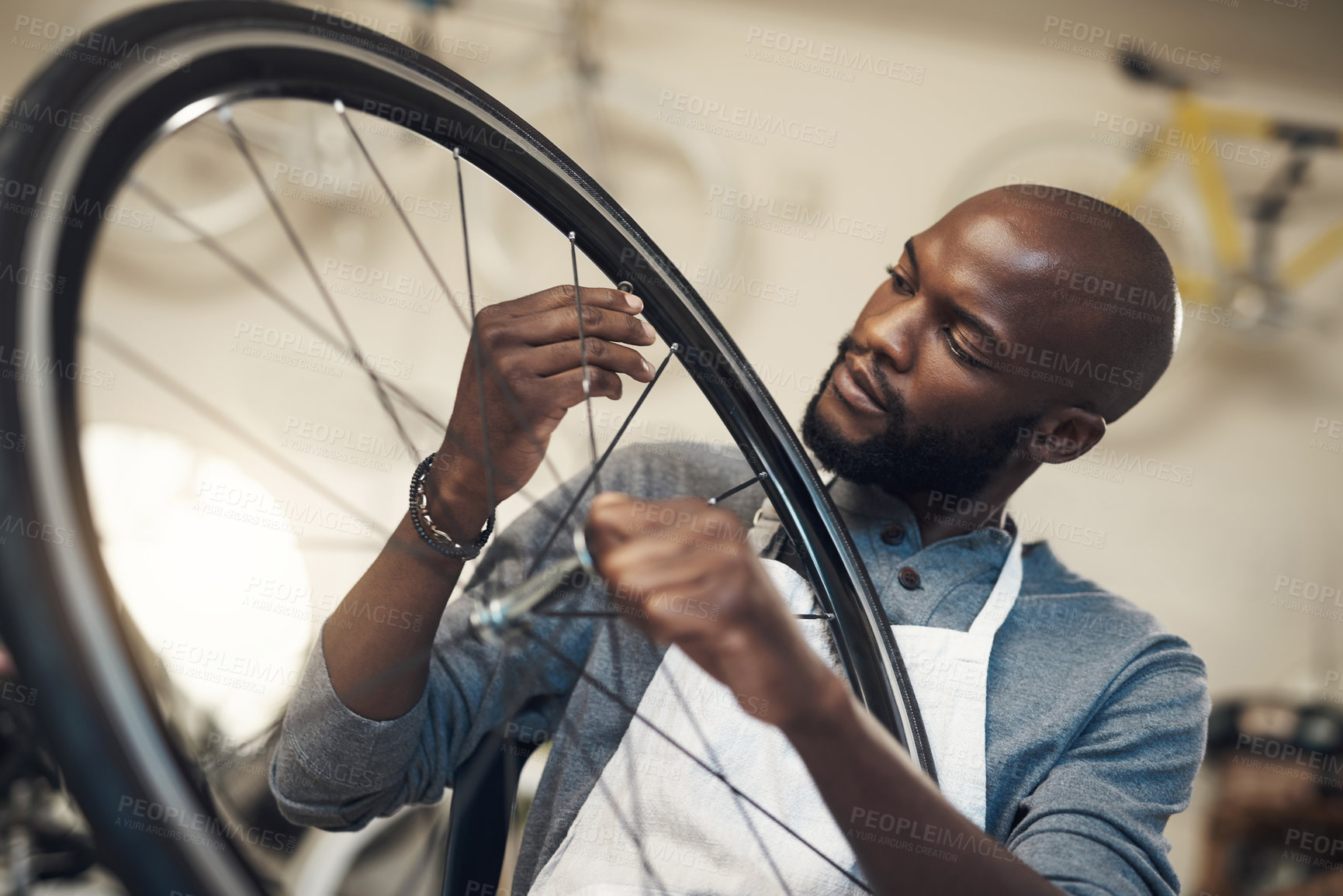 Buy stock photo Shot of a young man fixing a wheel at a bicycle repair shop