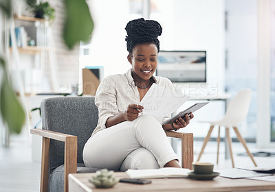 Buy stock photo Shot of a businesswoman using her digital tablet while reading paperwork