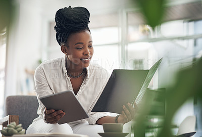 Buy stock photo Shot of a businesswoman using her digital tablet while reading paperwork