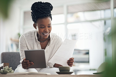 Buy stock photo Shot of a businesswoman using her digital tablet while reading paperwork