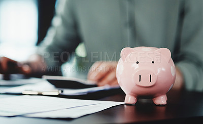 Buy stock photo Shot of an unrecognizable businessman doing paperwork with a piggybank on his desk at work
