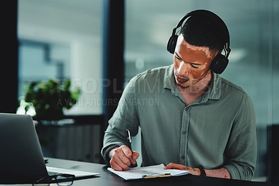 Buy stock photo Shot of a young businessman writing on a notepad in an office at work