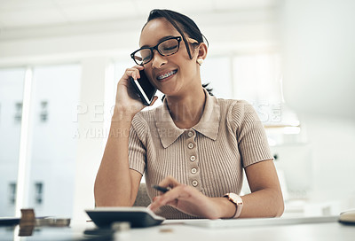 Buy stock photo Shot of a young businesswoman talking on a cellphone while calculating finances in an office