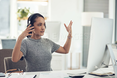 Buy stock photo Shot of a young businesswoman wearing headphones during a video call on a computer in an office