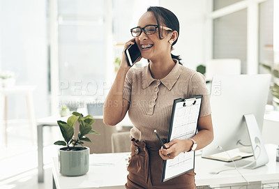 Buy stock photo Shot of a young businesswoman talking on a cellphone while holding a clipboard in an office