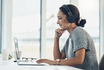 Buy stock photo Shot of a young businesswoman wearing headphones while working on a laptop in an office
