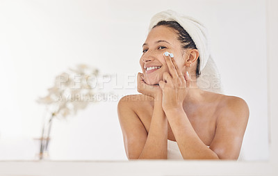 Buy stock photo Shot of an attractive young woman standing alone in her bathroom after a shower and applying face cream