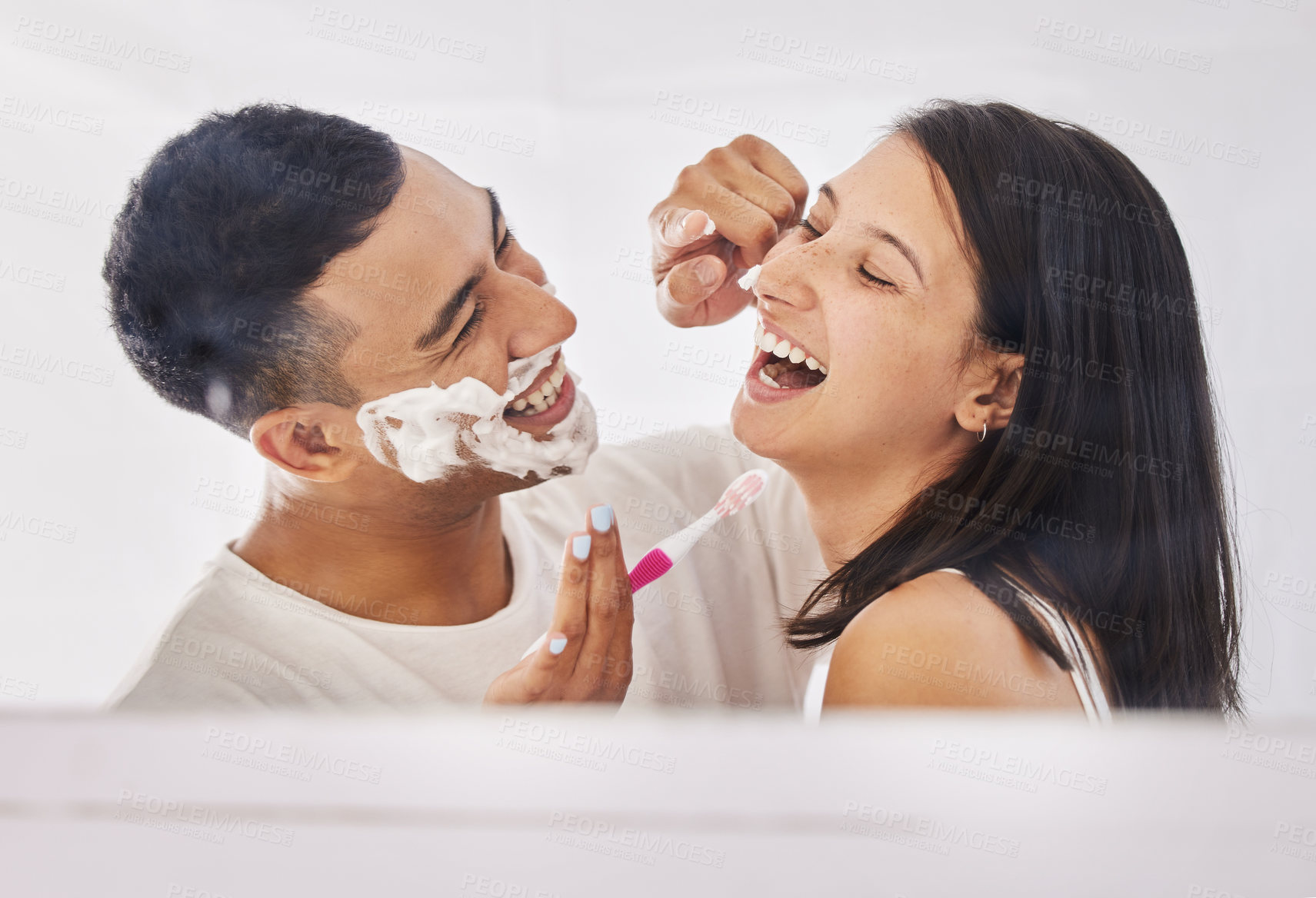 Buy stock photo Shot of a happy young couple standing together in their bathroom and feeling playful while shaving