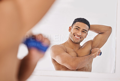 Buy stock photo Shot of a handsome young man standing alone in his bathroom and applying deodorant after his shower