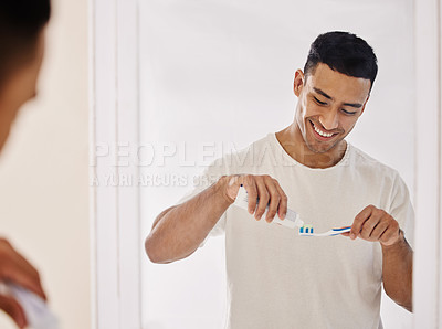 Buy stock photo Shot of a handsome young man standing alone in his bathroom and brushing his teeth in the morning