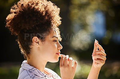 Buy stock photo Cropped shot of an attractive young woman applying lipstick while sitting in the park