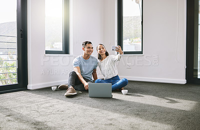 Buy stock photo Full length shot of a young couple sitting together and using a cellphone to take selfies in their new home