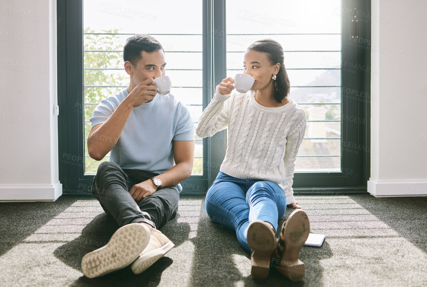 Buy stock photo Full length of a young couple sitting together in their new home and enjoying a cup of tea