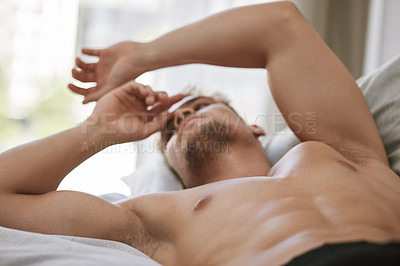 Buy stock photo Cropped shot of a handsome and muscular young man looking thoughtful while lying in his bed at home