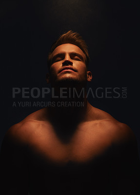 Buy stock photo Shot of a handsome young man with no shirt on standing in the shadows